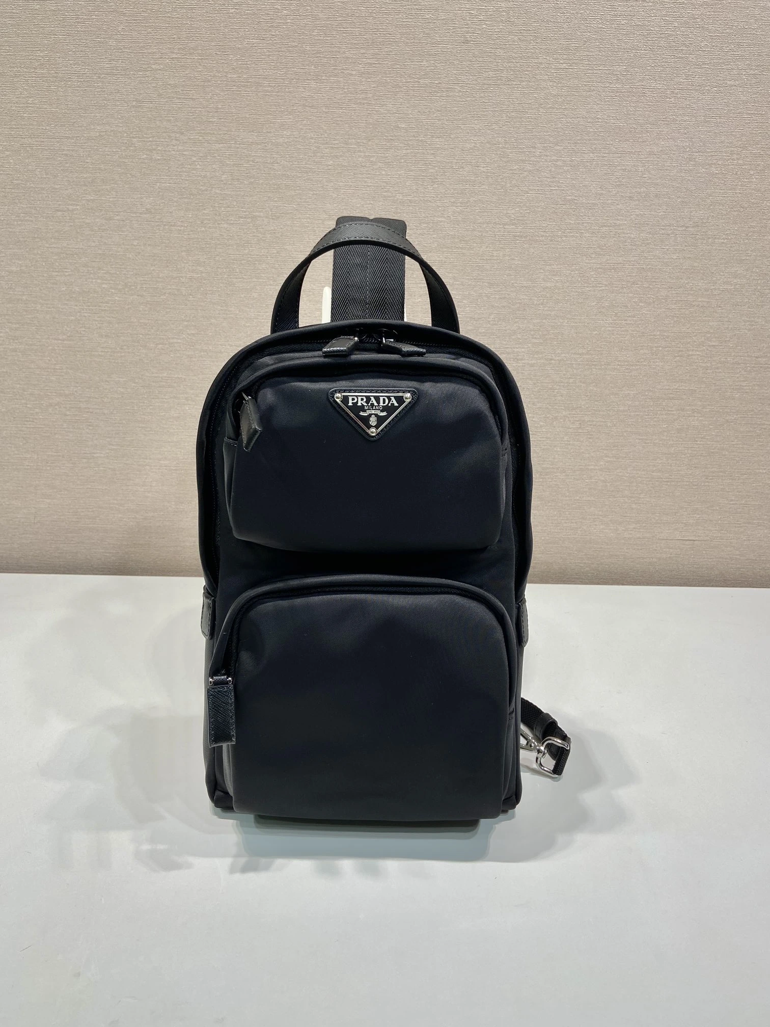 🎉新作クロスボディバッグ🎉2VZ105🎉🎉 このRe-Nylon(再生ナイロン)とサフィアーノレザーを使用したバッグは、モダンなショルダーバッグデザインを採用しています。レザーの持ち手と、調節可能なパッド入りナイロンストラップを備えています。前面にはエナメル加工された金属製の三角ロゴが施され、ファスナー開閉式です。外側にファスナー付きポケットが2つあり、収納