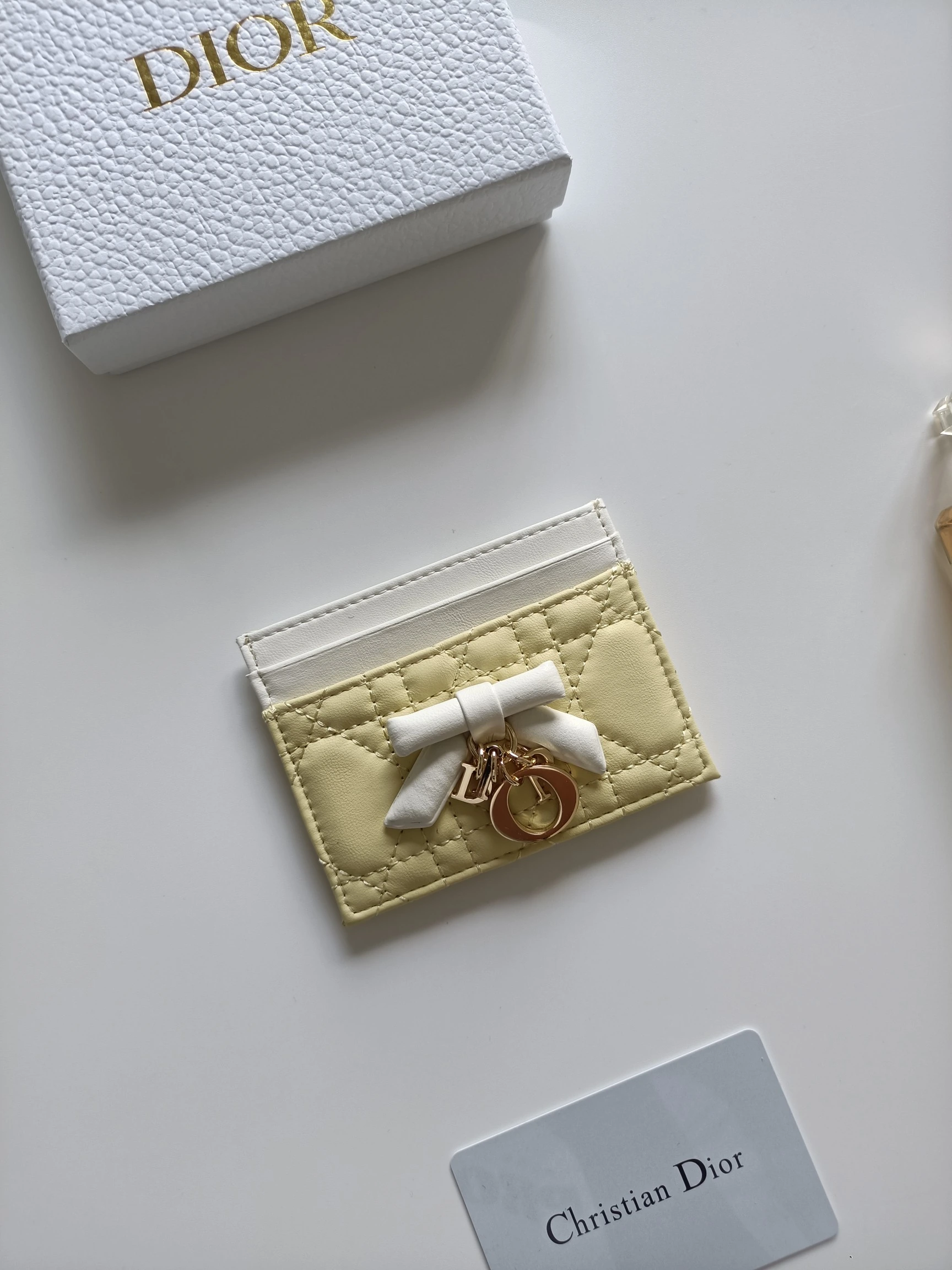 ディオールの最新作、商品番号：S2604 サイズ：10.5×8×0.5cm この「Lady Dior Freesia」カードケースは、エレガントで実用的なアクセサリーです。淡いピンク（Soupir pink）とクリーム色のツートンカラーで、ラムレザーを丁寧に仕立て、カギ目模様のステッチが施されています。前面には装飾用のレザーリボンがアクセントとなり、シルバー