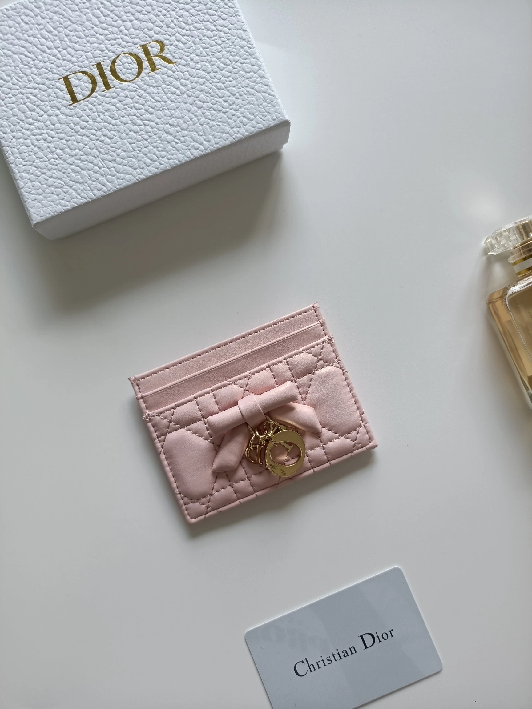 ディオールの最新作、商品番号：S2604 サイズ：10.5×8×0.5cm この「Lady Dior Freesia」カードケースは、エレガントで実用的なアクセサリーです。淡いピンク（Soupir pink）とクリーム色のツートンカラーで、ラムレザーを丁寧に仕立て、カギ目模様のステッチが施されています。前面には装飾用のレザーリボンがアクセントとしてあしらわれ