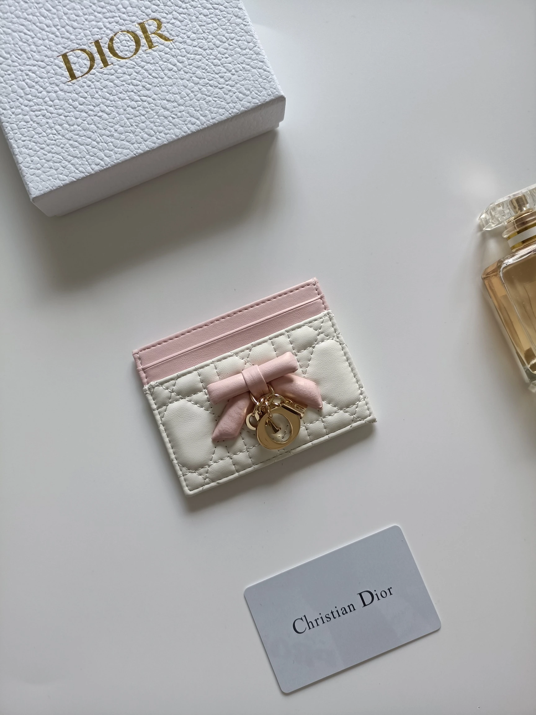 ディオールの最新作、商品番号:S2604 サイズ:10.5×8×0.5cm この「Lady Dior Freesia」カードケースは、エレガントで実用的なアクセサリーです。淡いピンク(Soupir pink)とクリーム色のツートンカラーで、ラムレザーを丁寧に仕立て、カギ目模様のステッチが施されています。前面には装飾用のレザーリボンがアクセントとしてあしらわれ